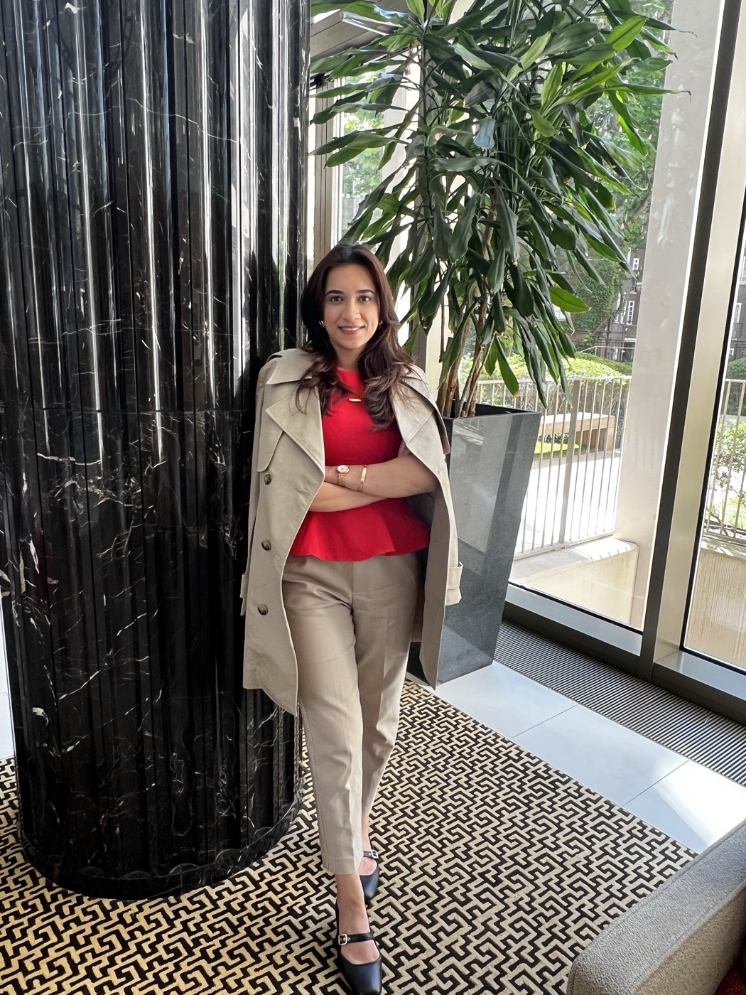 Shreya Gulati in London, red top and trench coat by a marble column
